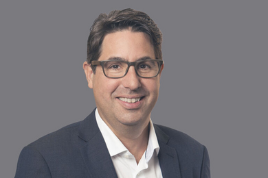 Porträt lächelnder Mann mit Brille in Anzug und Hemd.