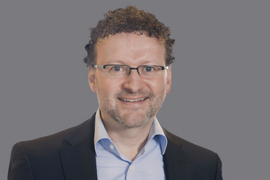 Porträt lächelnder, lockiger Mann mit Brille. 