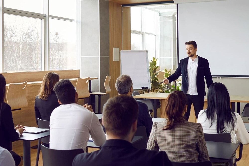 Mann hält Vortrag mit Flipchart vor mehreren Personen, die auf Stühlen sitzen