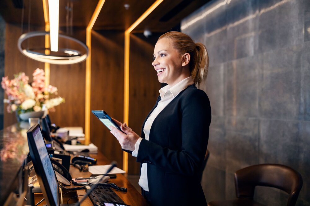 Eine junge Rezeptionistin im seitlichen Profi an der Rezeption mit einem iPad in der Hand