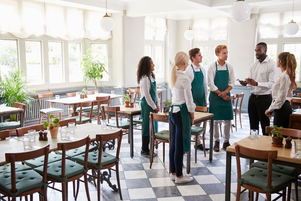 Eine Gruppe Kellner stehen für ein Meeting in einem Halbkreis in einem leeren Restaurant