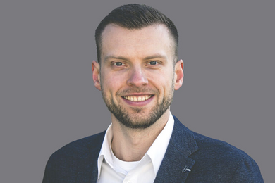 Porträt dunkelhaariger, lächelnder Mann in Anzug und Hemd. 