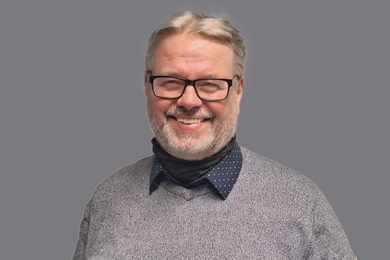 Porträt grauhaariger, lächelnder Mann mit Brille. Hemd und Pullover.