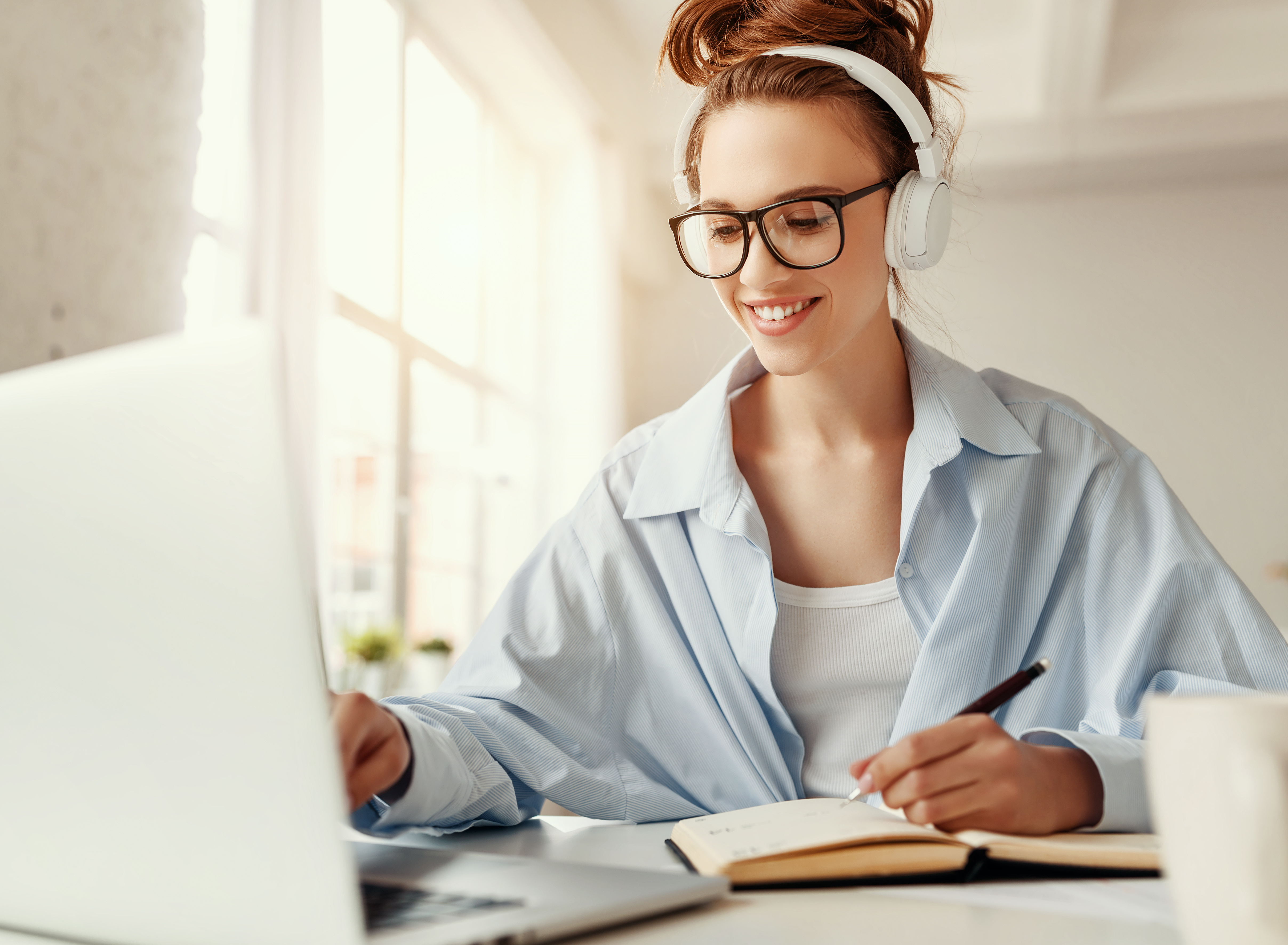 Junge Frau mit Kopfhörern vor einem aufgeklappten Laptop