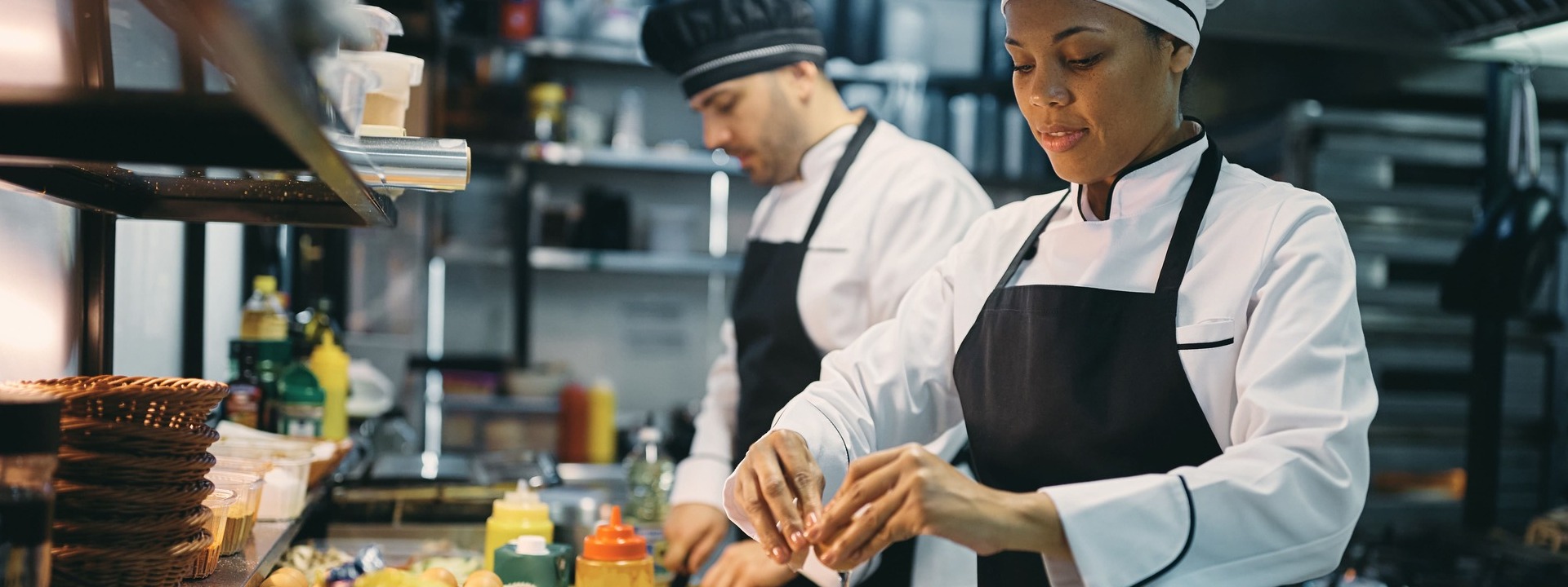 Zwei Köche mit Schürze und Kochjacken und -mütze in der Küche 