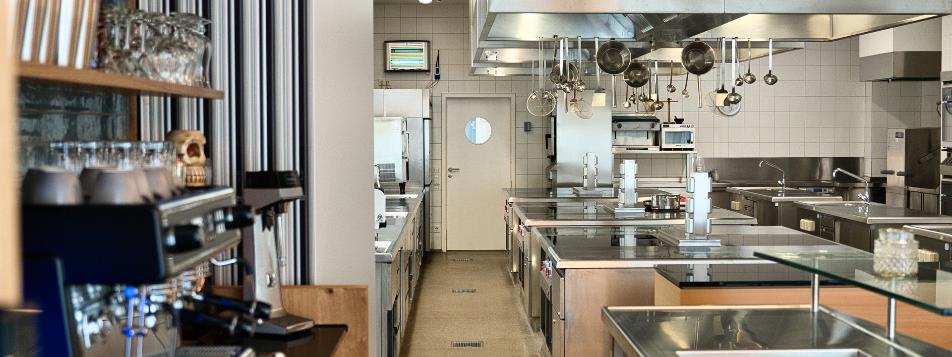 Blick von einer Bar in eine Küche. Links im Vidergrund eine Siebträgermaschine, rechts der Tresen