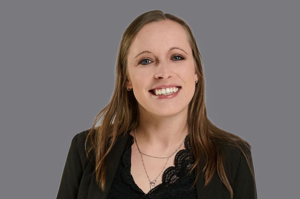 Lächelnde, braunhaarige Frau. Schwarzes Oberteil. 