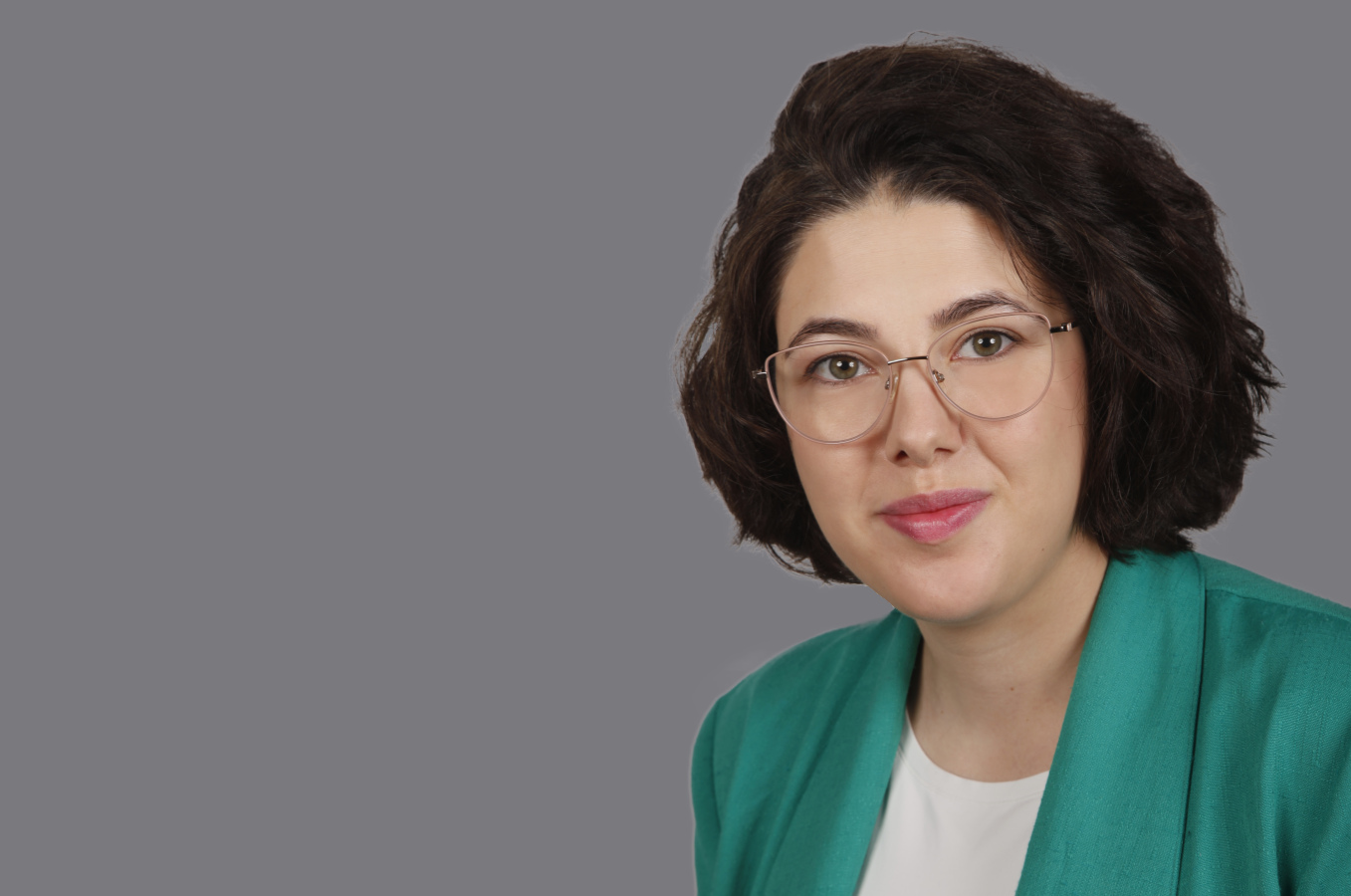 Lächelnde braunhaarige Frau mit Brille und grünem Blazer 