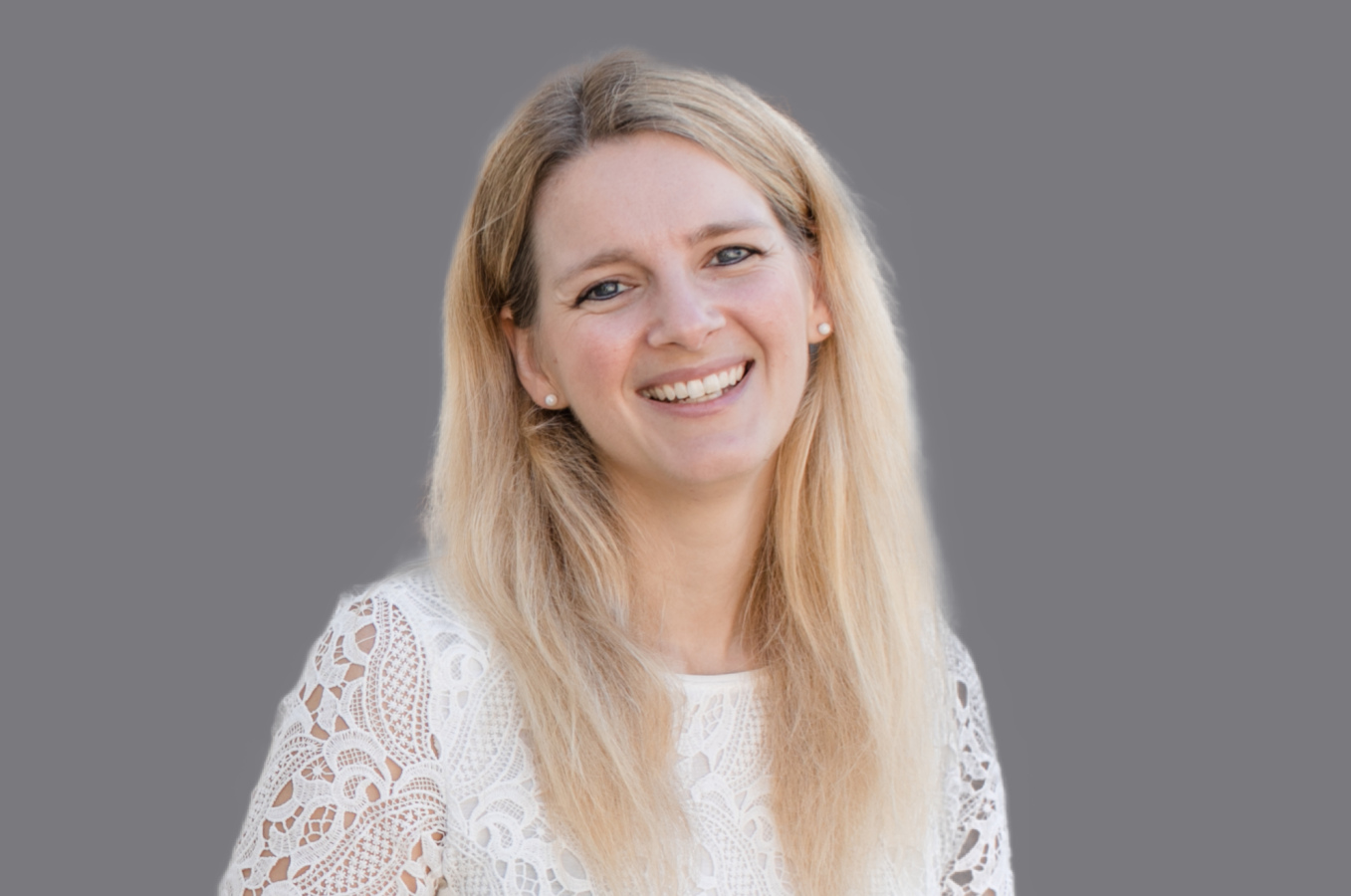 Lachende, blonde Frau mit offenen Haaren und weißem Oberteil 